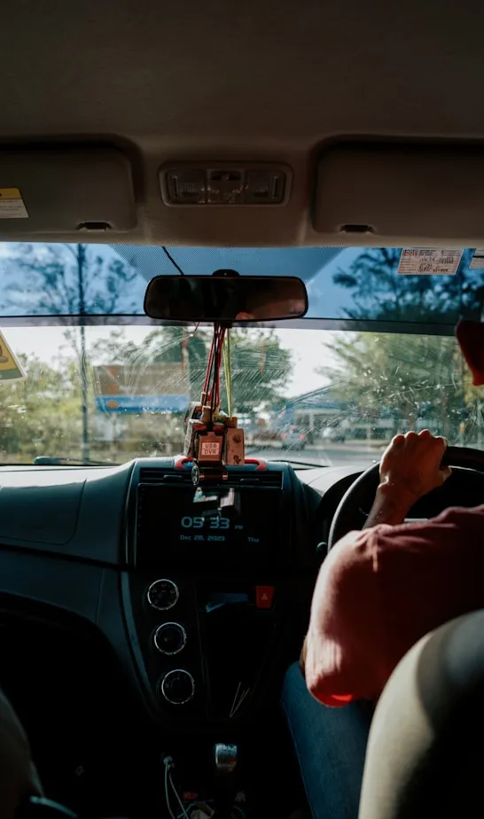 A car interior viewed from the back seat, with the dashboard display showing the time and date and sunlight streaming through the windscreen.