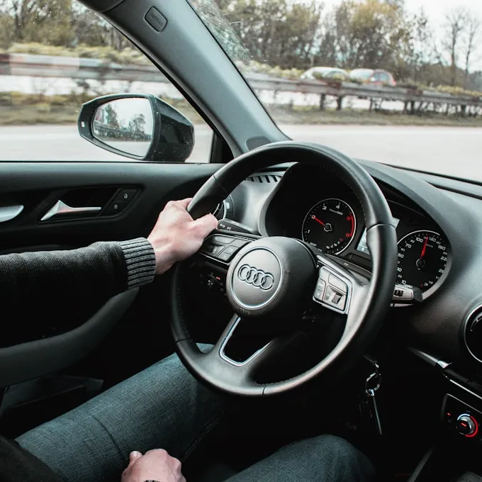 A person driving with their left hand on the steering wheel, a speedometer and GPS map visible on the dashboard.